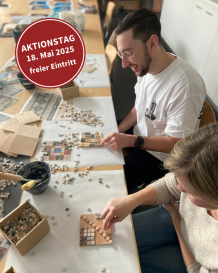Zwei Personen sitzen an einem Tisch und legen kleine Mosaiken.
